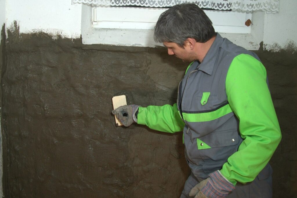 Verwerker brengt afdichtingsslurry met de spaan aan op een kelderwand onder het keldergat