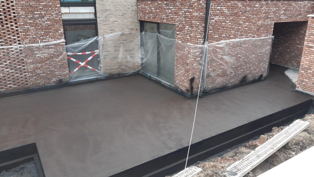 Verse werkvloer op de binnenplaats, met afgeplakte plint en een afvoergoot langs de rand